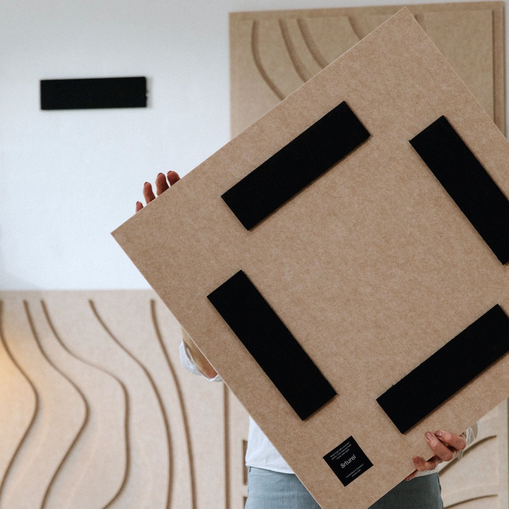 Person holding a sand-colored acoustic art panel from Arturel, showing the back mounting system for easy installation.